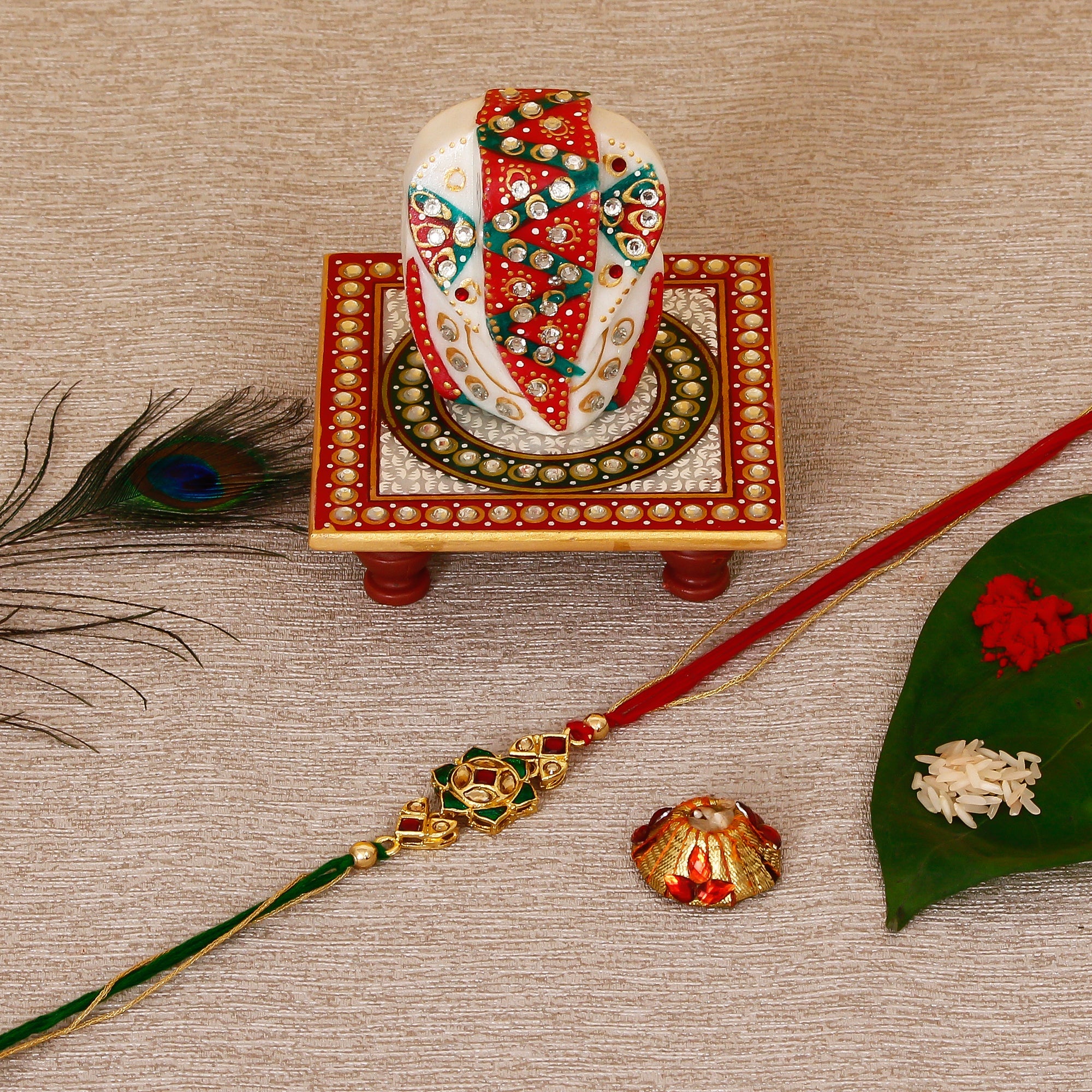 Designer Kundan Rakhi with Lord Ganesha on Kundan Studded Marble Chowki and Roli Tikka Matki Kafalo