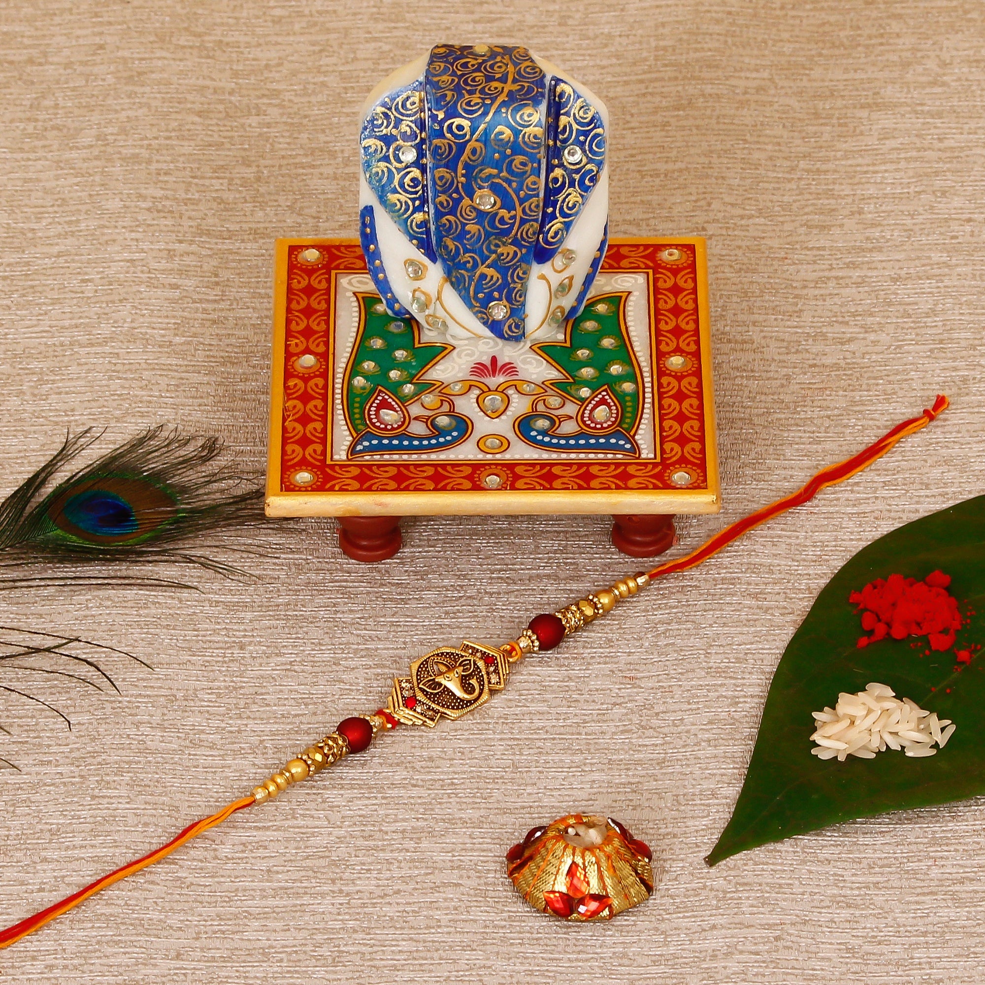 Designer Religious Ganesha Rakhi with Lord Ganesha on Marble Chowki and Roli Tikka Matki Kafalo